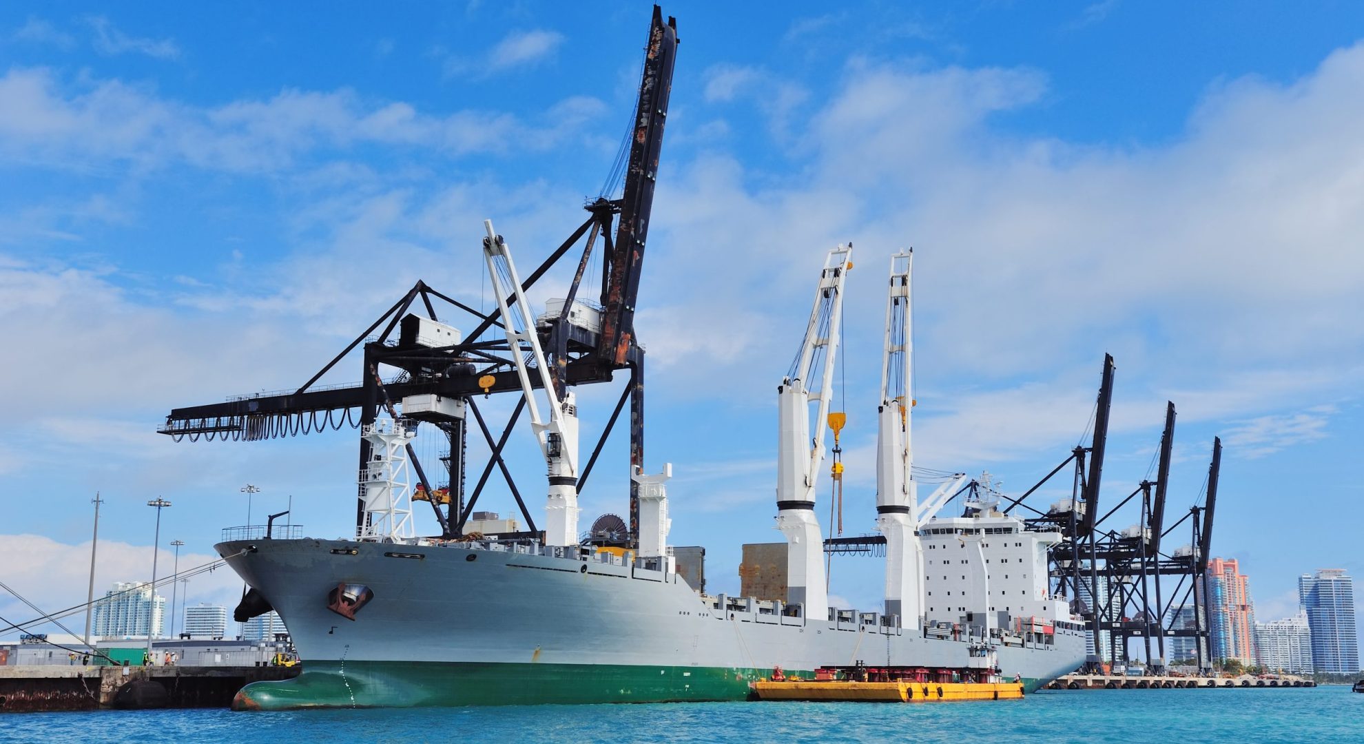 Cargo ship at Miami harbor with crane and blue sky over sea.